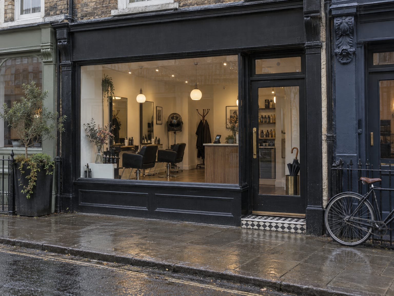 The glass front door of a small hair salon on a wet high street, styling chairs visible through the window