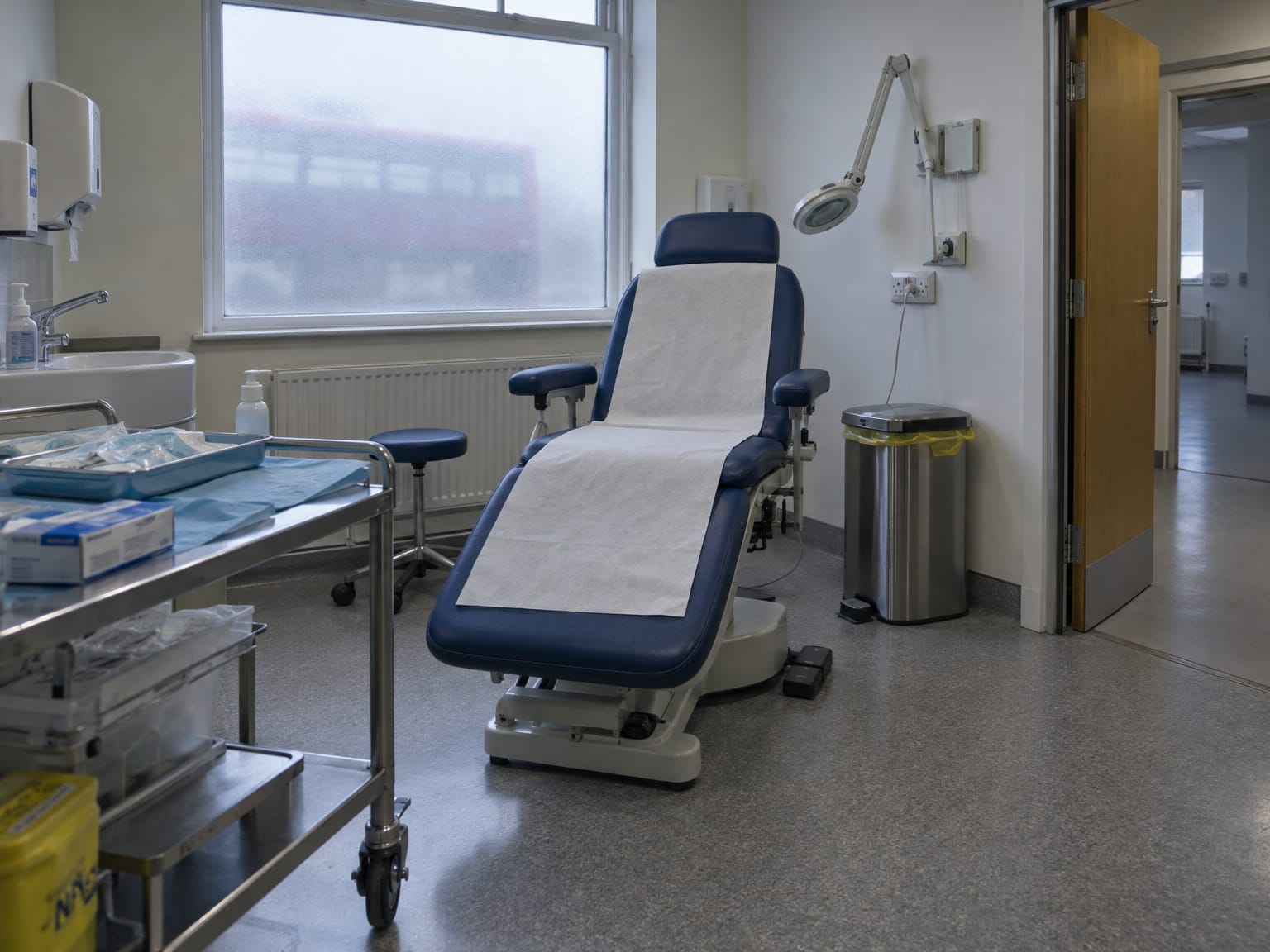 An empty podiatry room, a reclining chair and a steel instrument trolley under a magnifier lamp